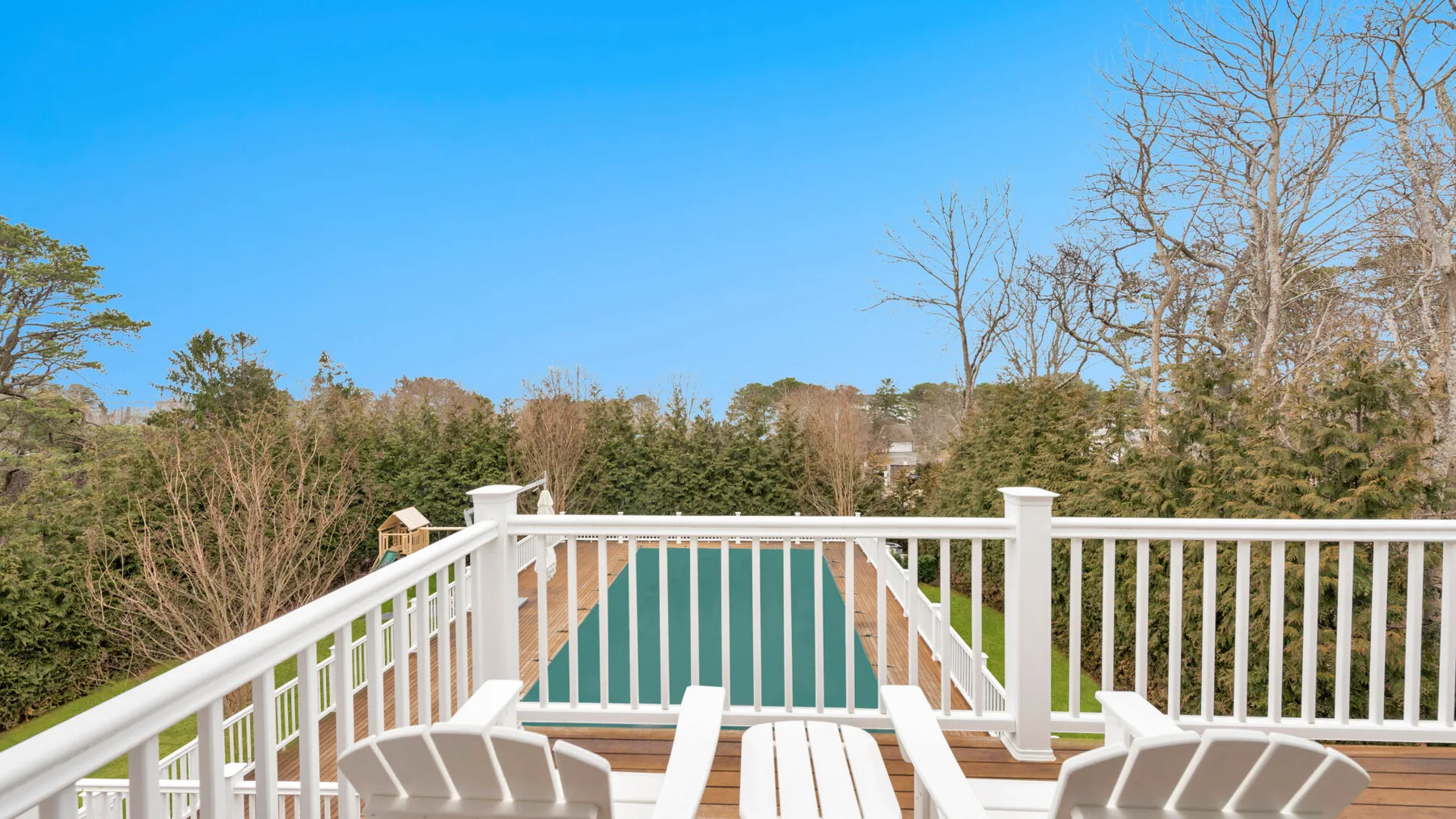 A wooden deck overlooks a turquoise swimming pool, with outdoor seating in the foreground.