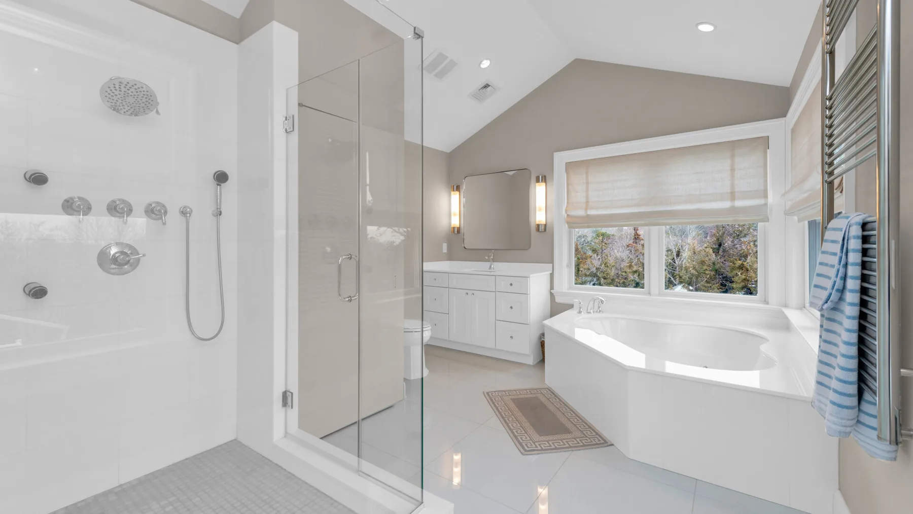 A bright bathroom features a glass shower, vanity, and bathtub beside a window.