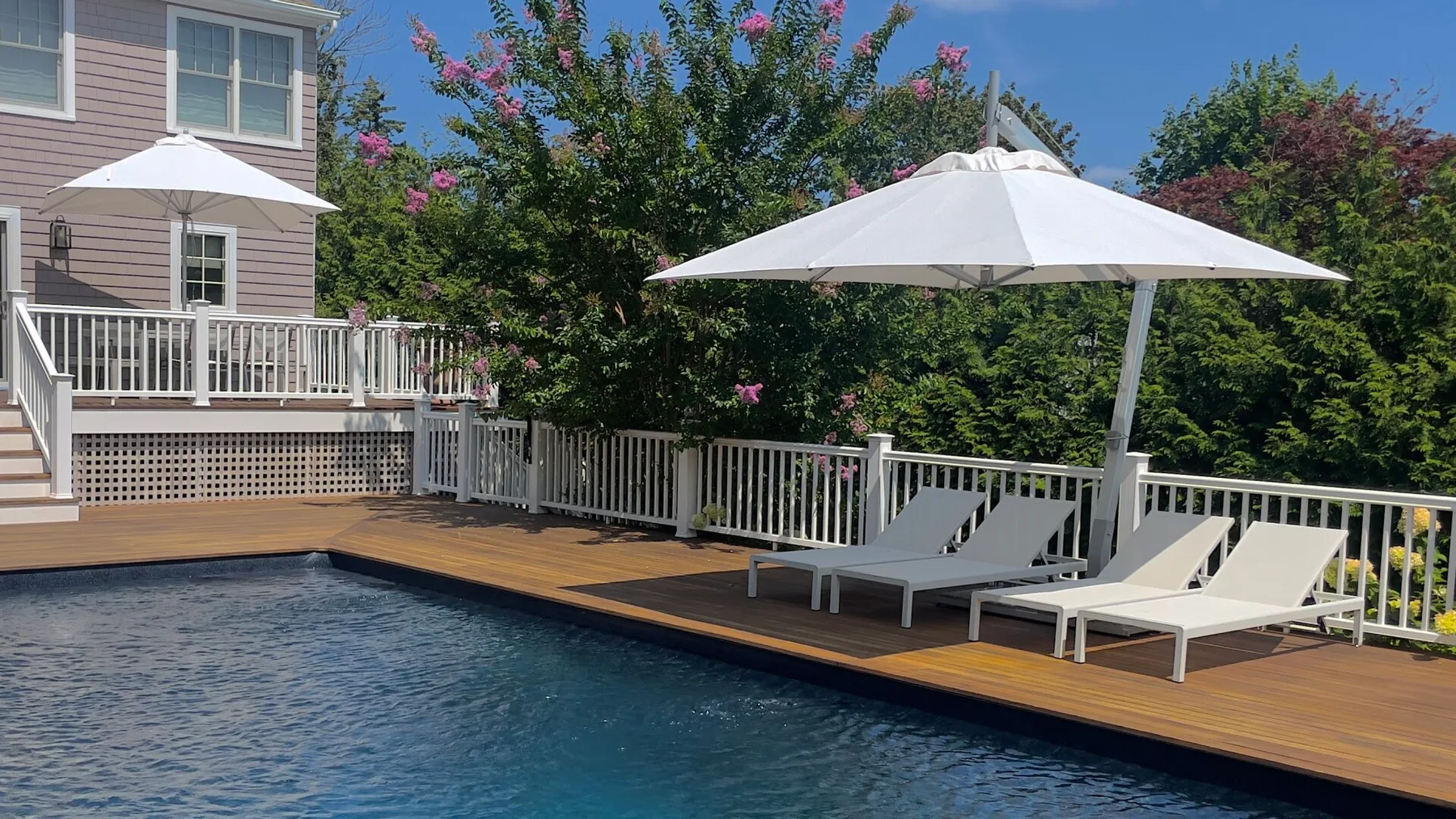 An outdoor swimming pool beside a wooden deck with lounge seating and umbrellas.