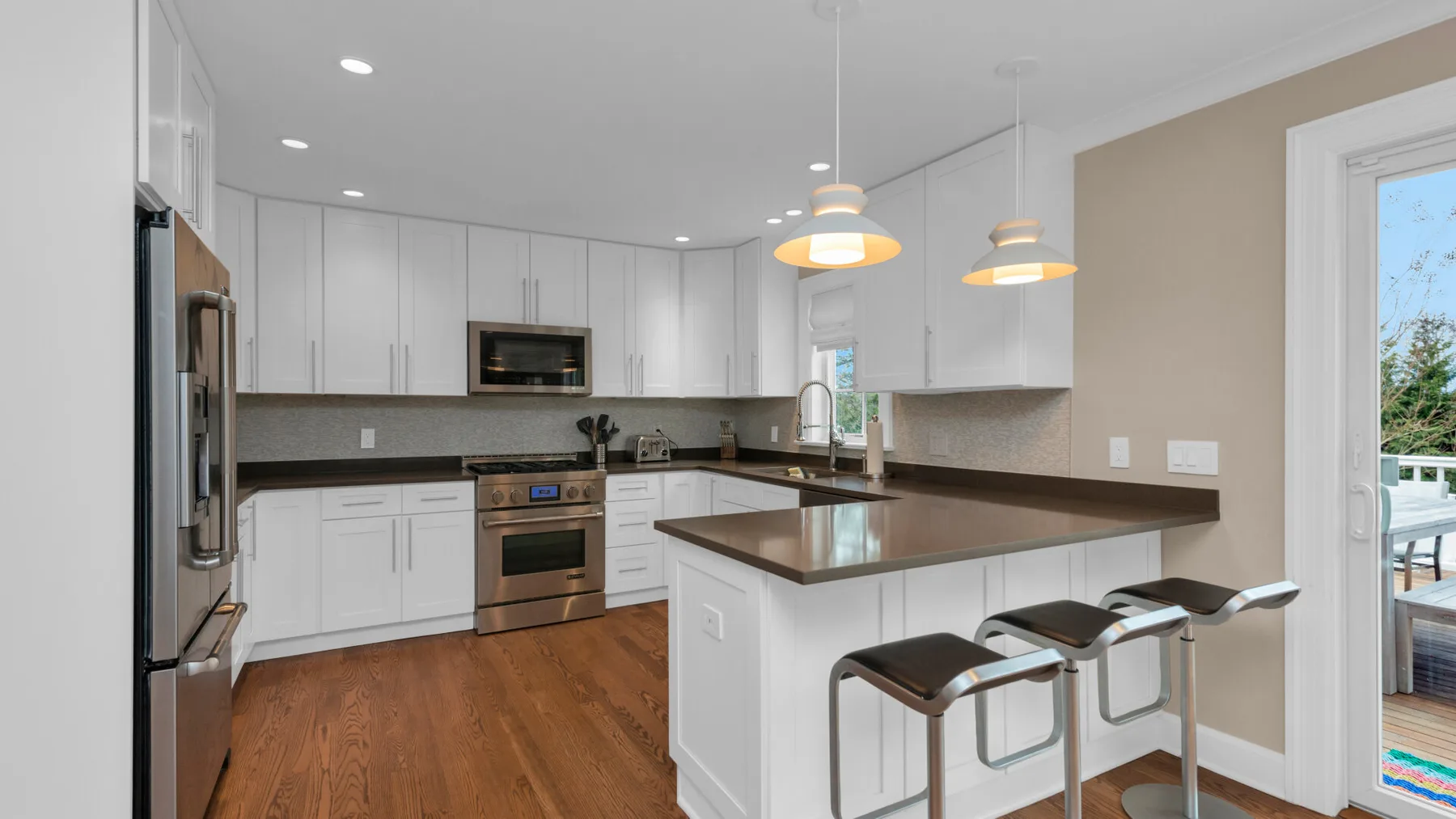 A bright kitchen with white cabinets, dark countertops, and seating at the island.