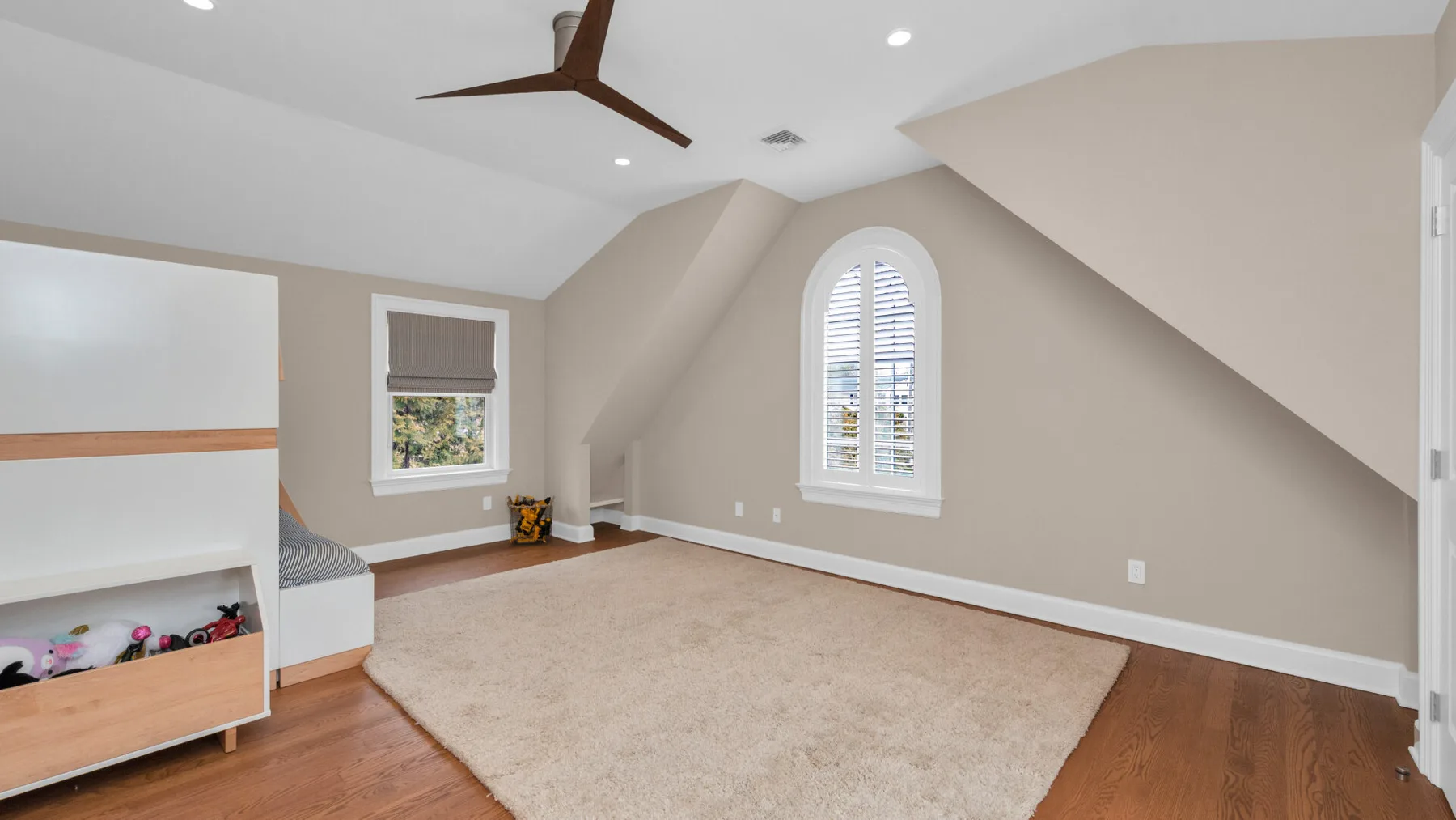 A bright attic bedroom with a large area rug and windows with blinds.