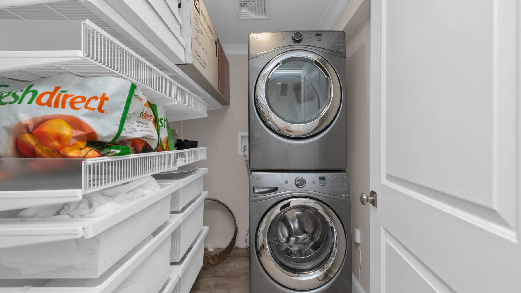 A laundry room with a stacked washer and dryer beside storage shelves.