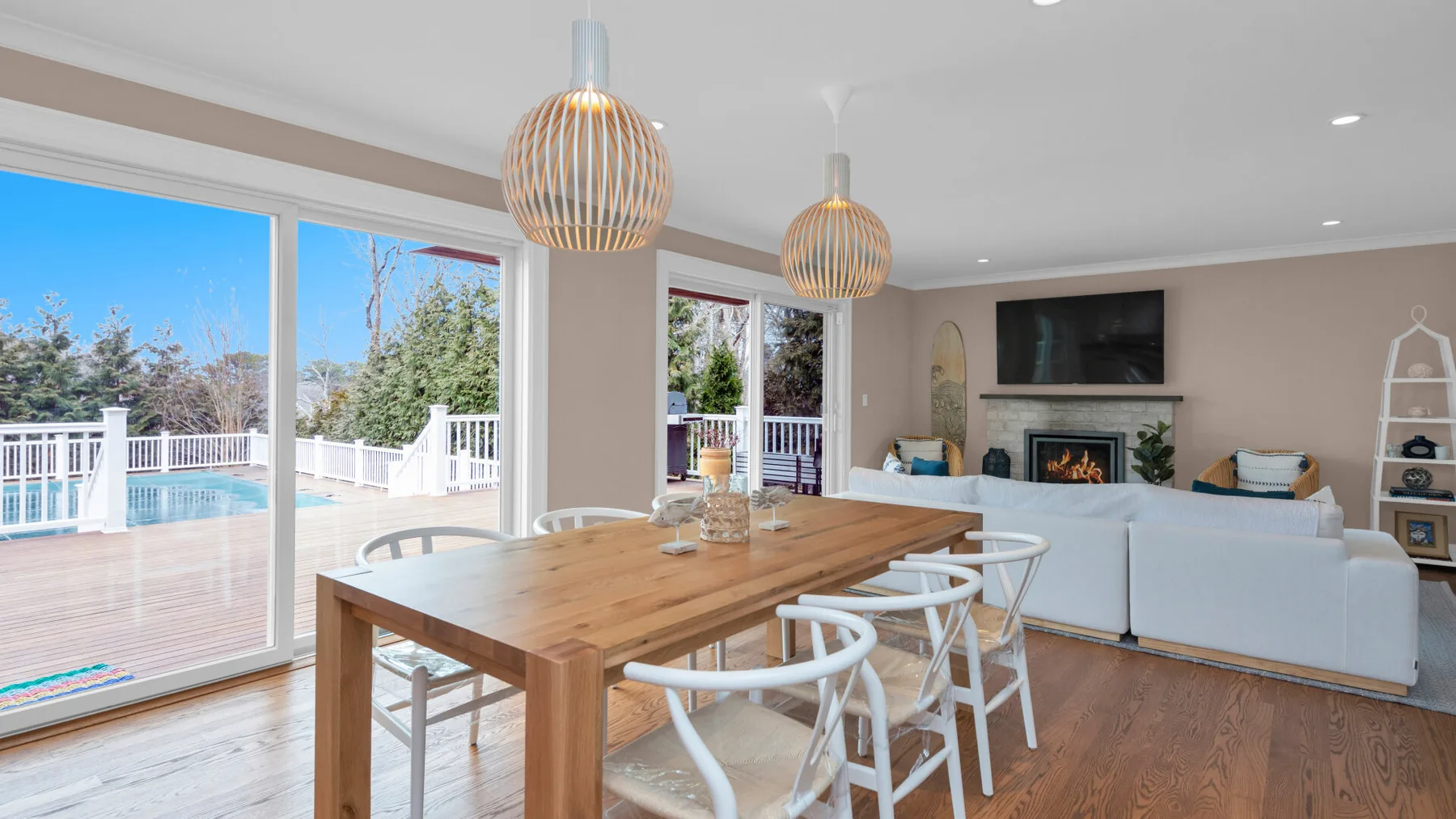 A bright open-plan living and dining area with a wooden table and large windows.
