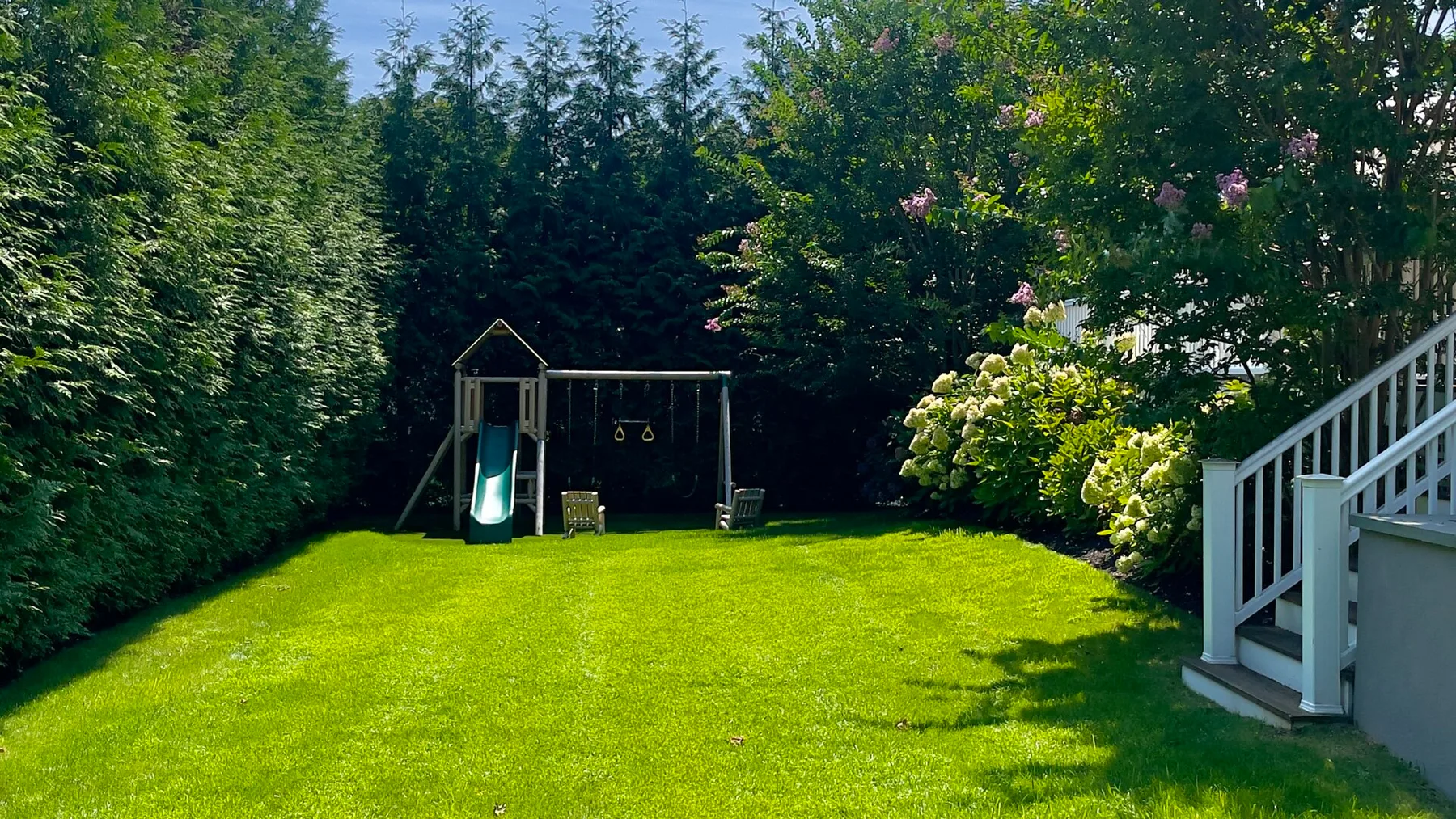A grassy backyard with a play structure and garden stairs.