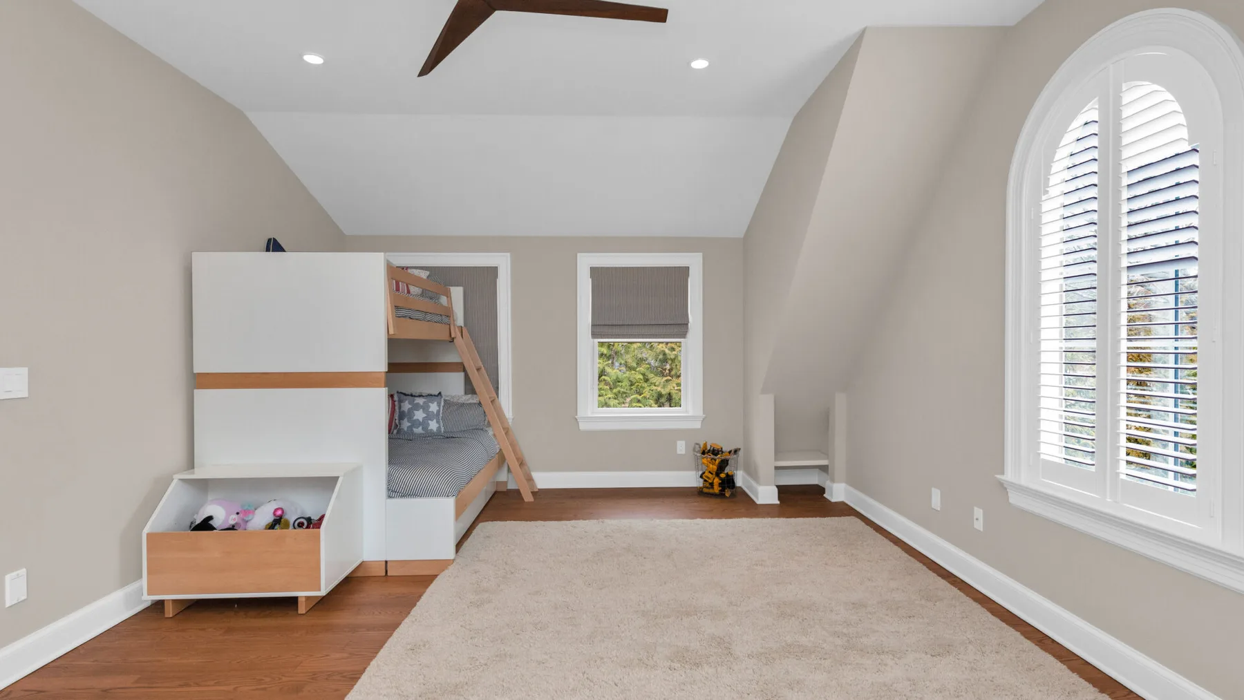 A bedroom with a loft bed, a large rug, and a tall arched window.