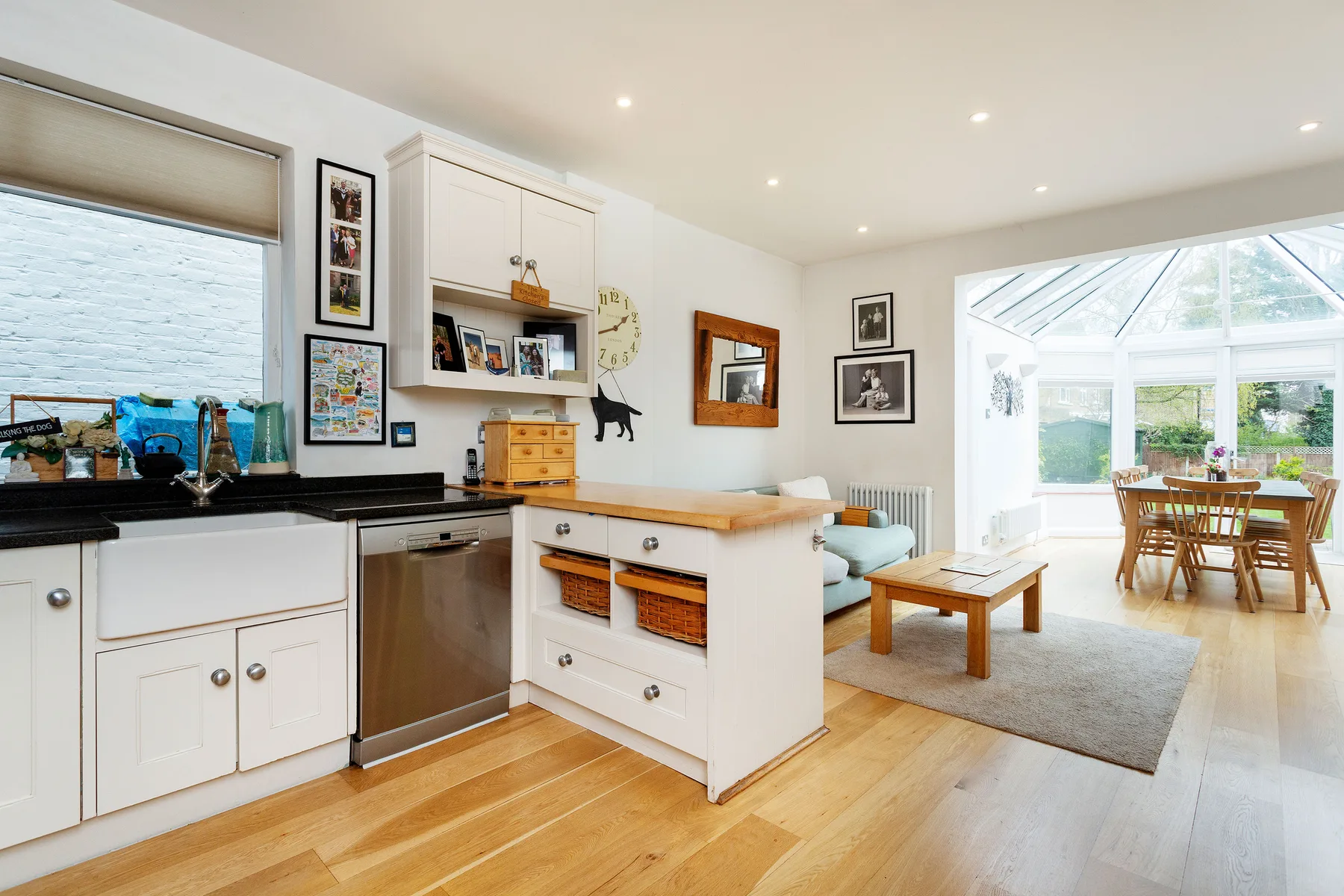 A bright open-plan kitchen and dining area with white cabinetry and a sunlit conservatory.