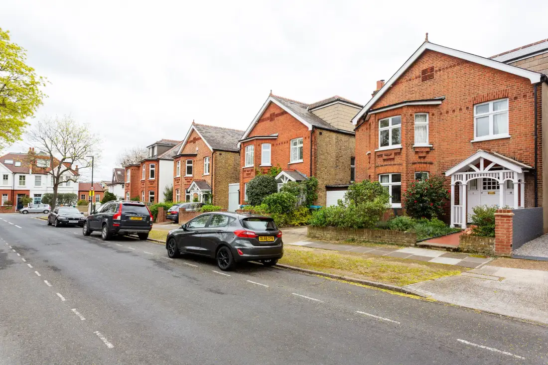 A residential street lined with brick houses and parked cars.