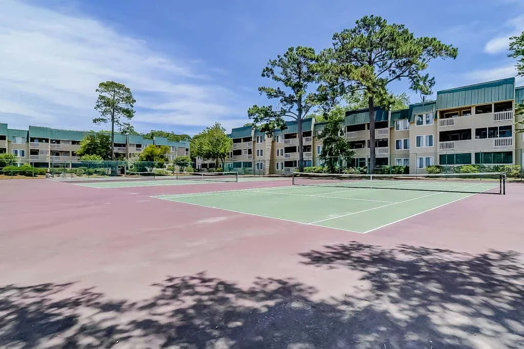 An outdoor tennis court sits in front of a multi-story residential building.