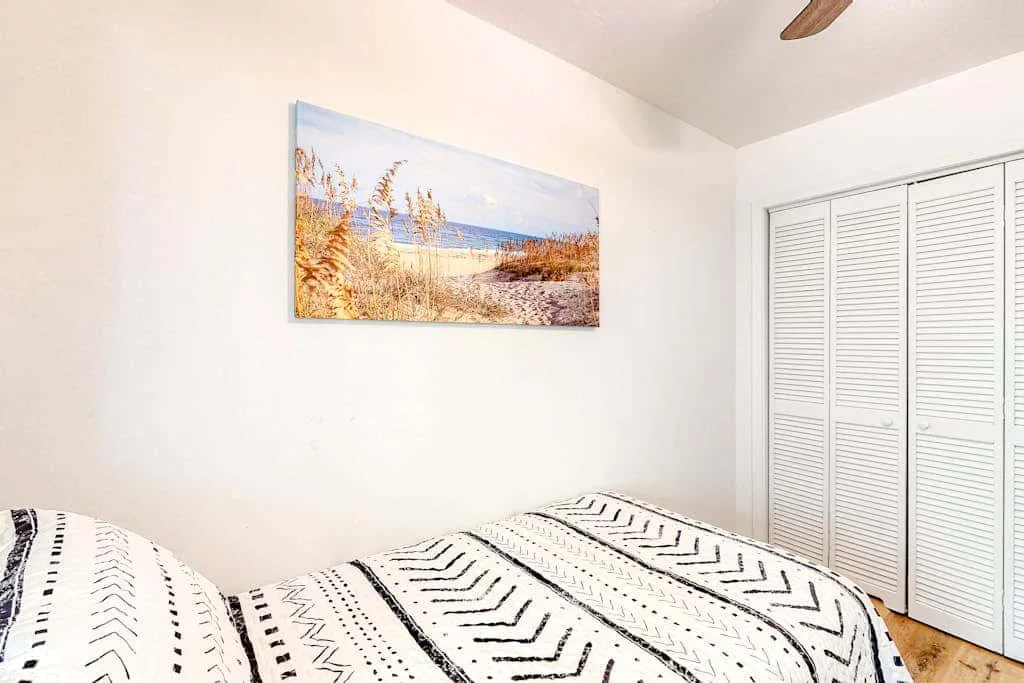 A bedroom with patterned bedding and a beach landscape picture on the wall.