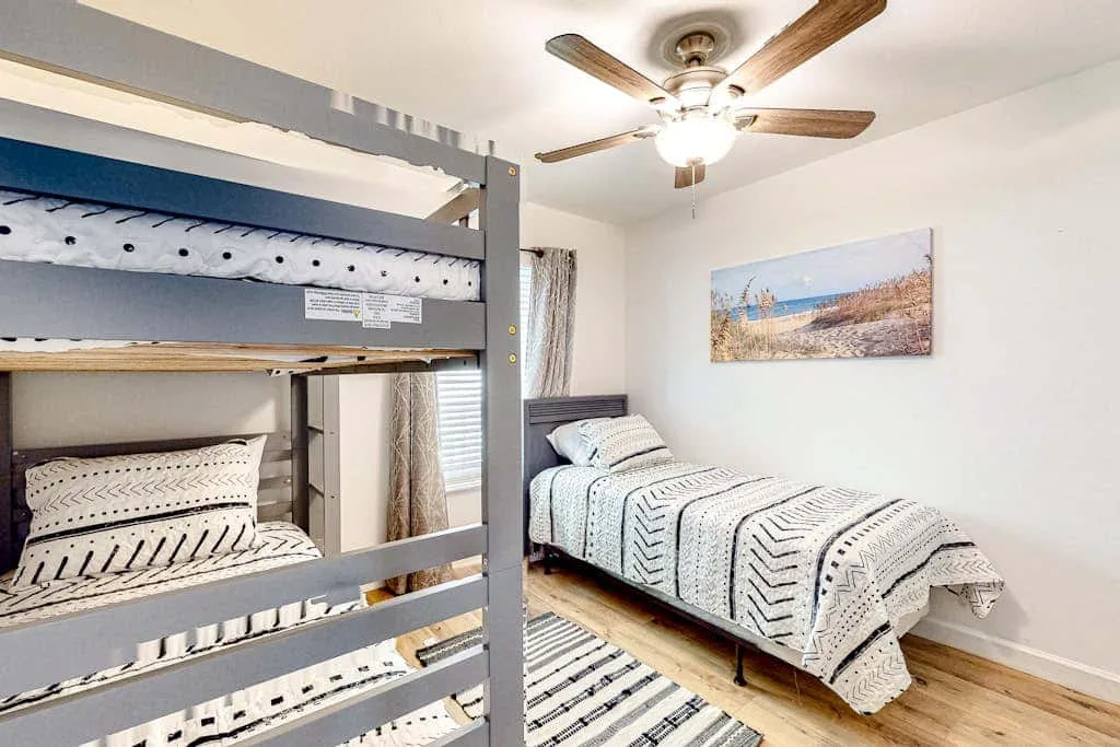 A bright bedroom with bunk beds and a single bed dressed in patterned bedding.