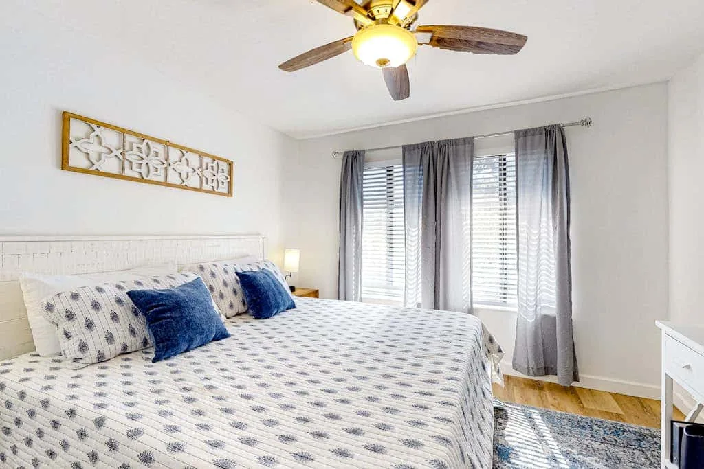 A bedroom with a patterned bed, blue pillows, and curtained windows.