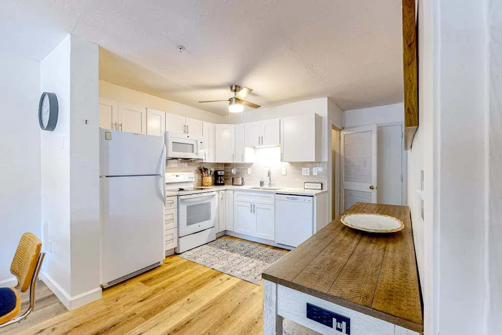 A bright kitchen with white cabinets and a wooden counter.