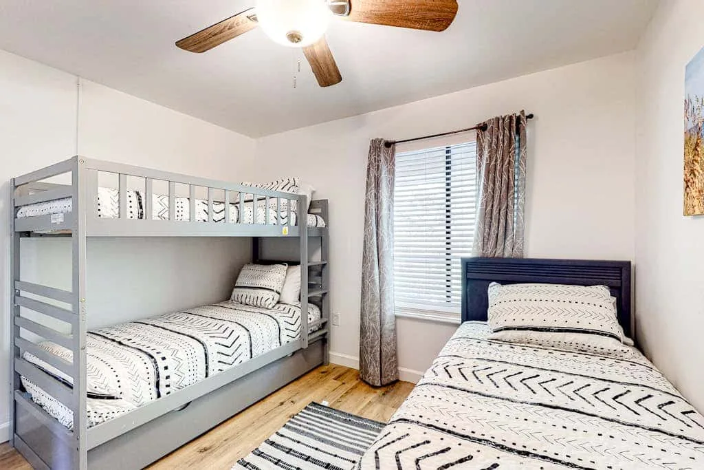 A bedroom with a gray bunk bed and a separate bed beside a window.