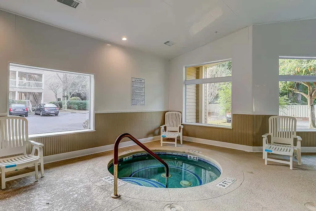 An indoor pool area with a small circular pool and seating beside the windows.