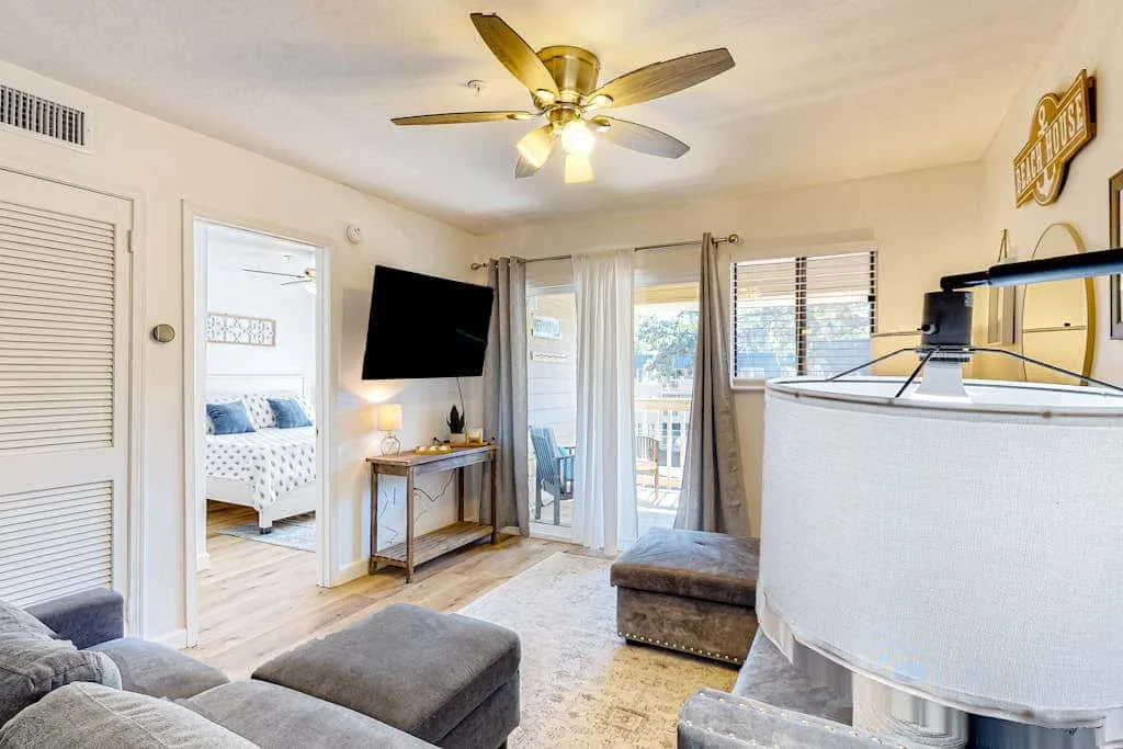 A bright living room with a ceiling fan, television, and sliding glass doors.
