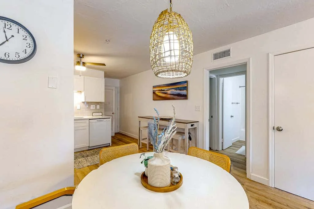 A bright dining area with a round table, woven pendant light, and compact kitchen.