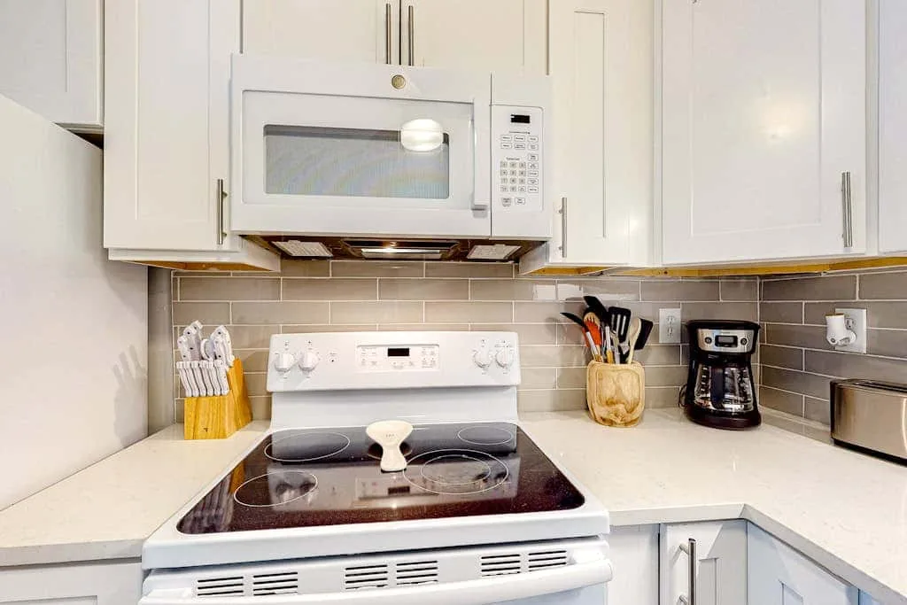 A bright kitchen with a stovetop, microwave, and white cabinetry.