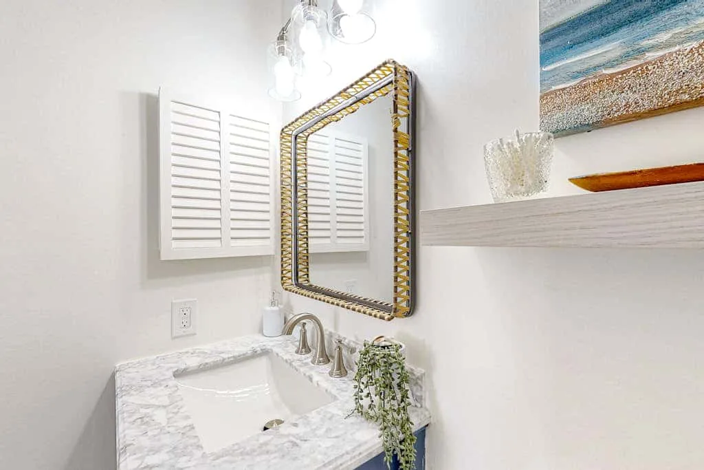 A bathroom vanity with a framed mirror and white shuttered windows.