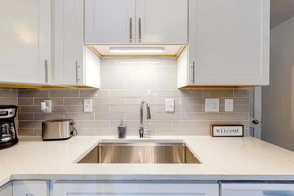 A bright kitchen counter with a stainless-steel sink beneath white cabinets.
