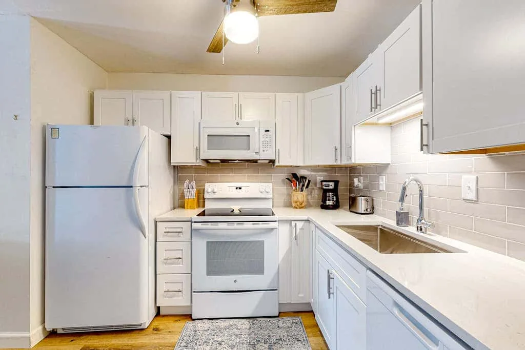 A bright kitchen with white cabinets, appliances, and a sink along the counter.