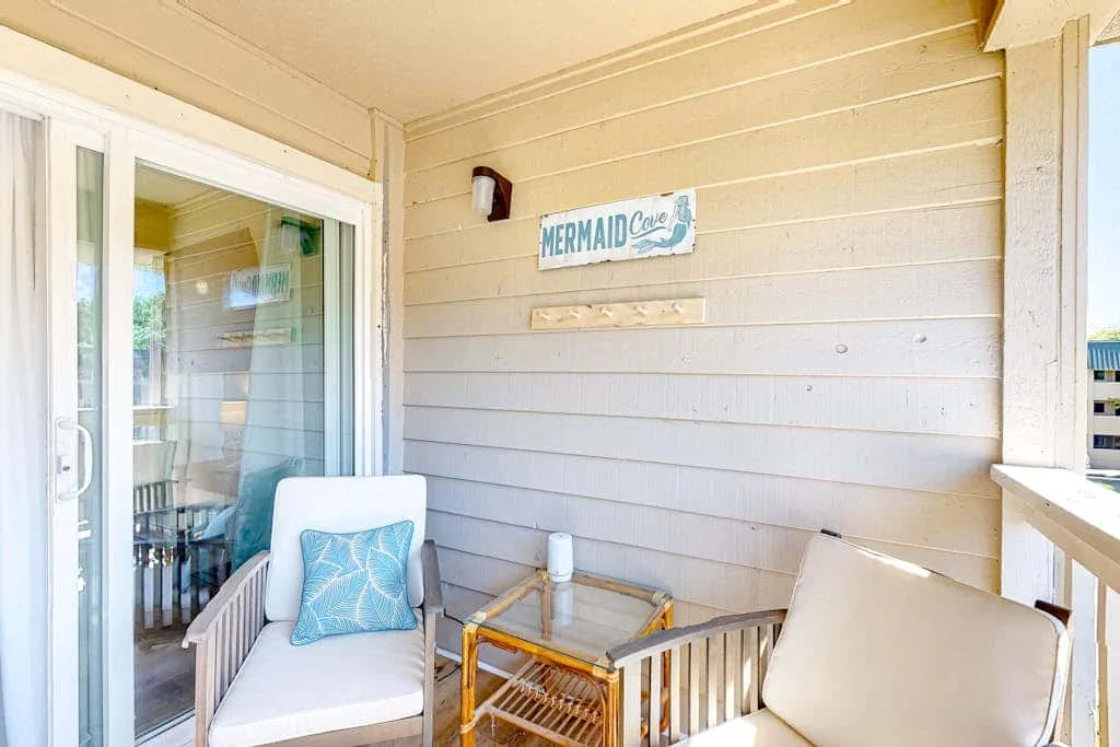 A covered porch has cushioned seating beside a sliding glass door.