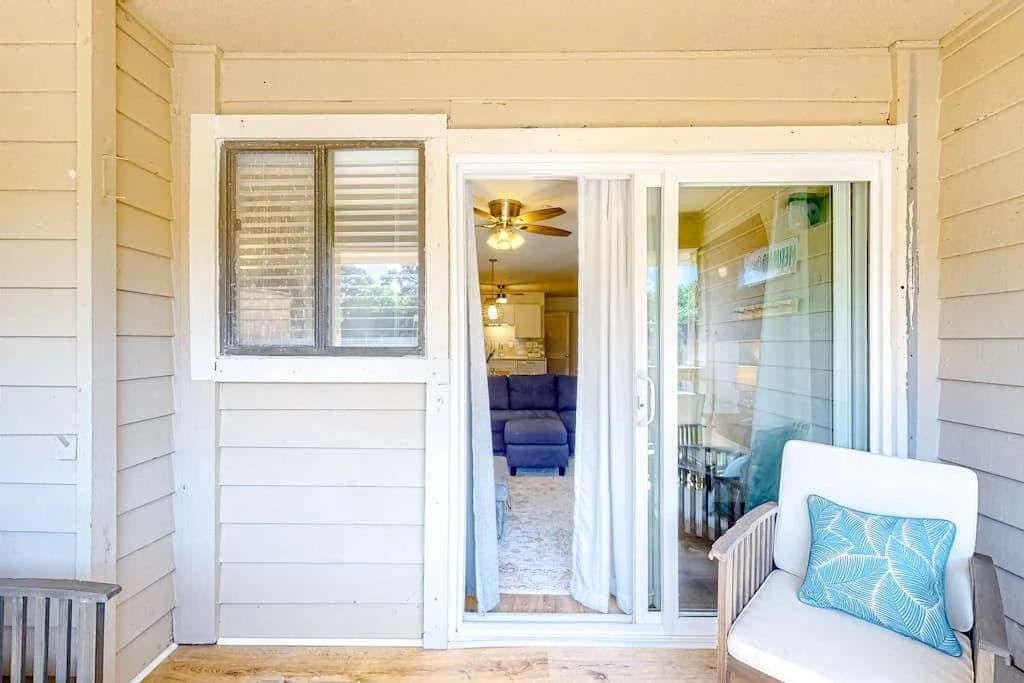 A covered porch with a cushioned seat beside sliding glass doors.