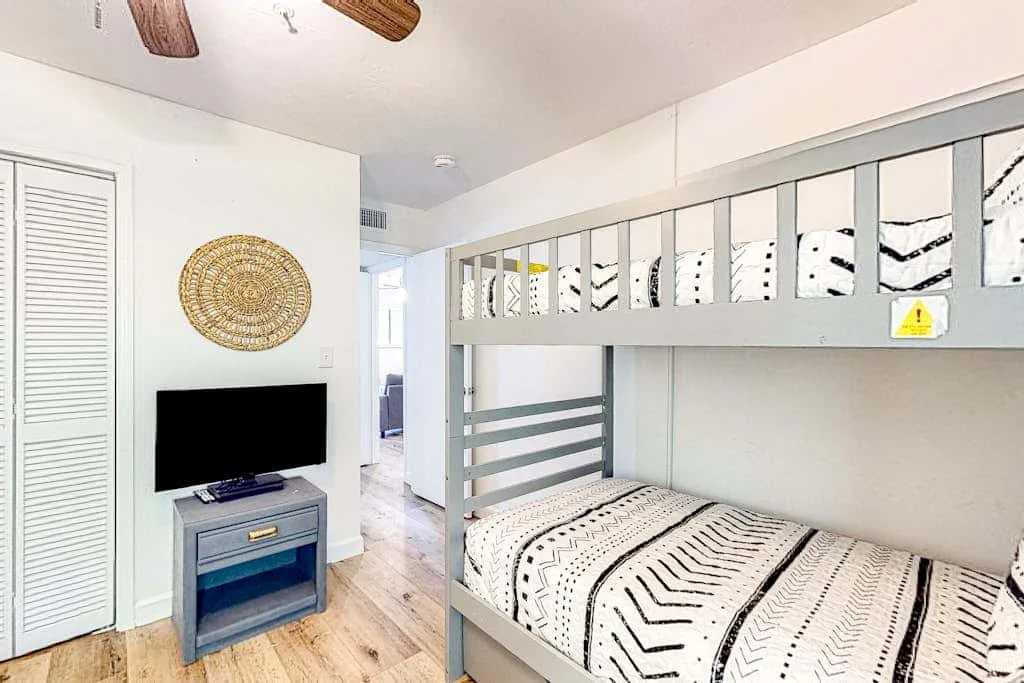 A bedroom with a gray bunk bed, patterned bedding, and a wall-mounted television.