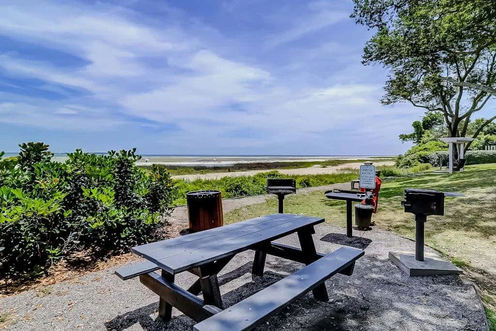 An outdoor picnic area with a table, grill, and ocean view.