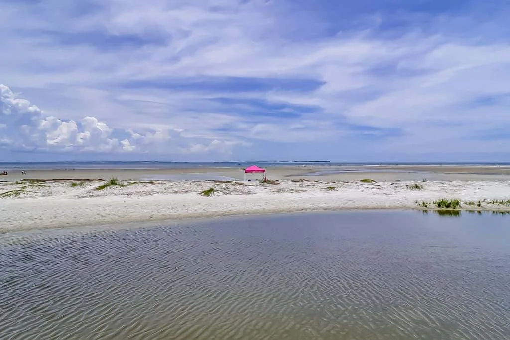 A sandy beach and shallow water sit beneath a broad, cloudy sky.