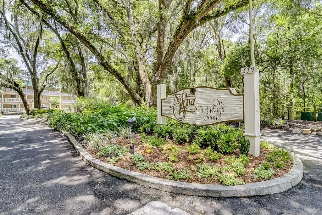 A landscaped entrance sign stands beside a tree-lined driveway.