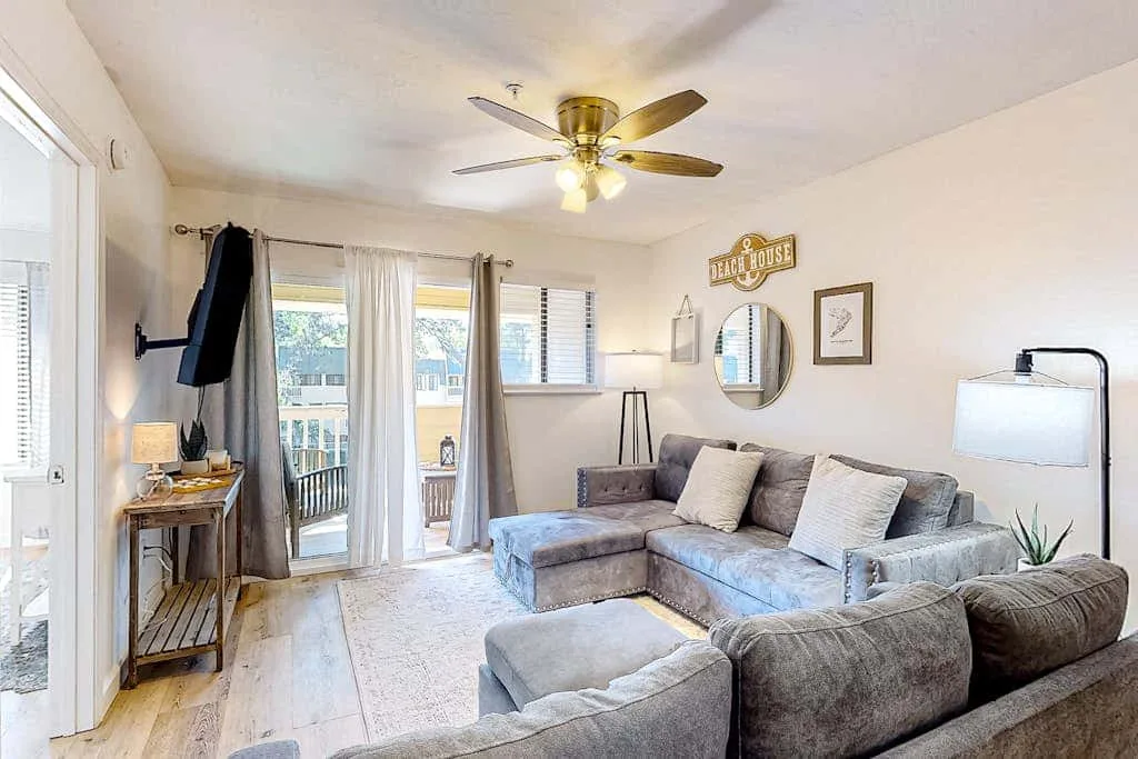 A bright living room with sectional seating and glass doors opening onto a balcony.