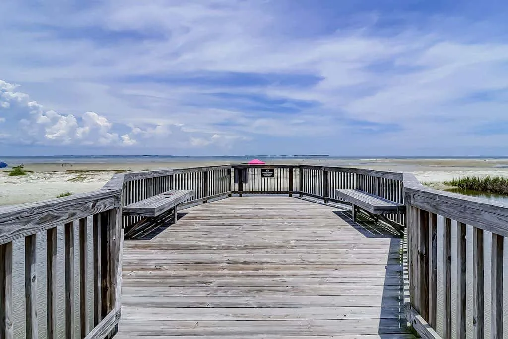 A wooden boardwalk leads across a sandy beach toward the shoreline.