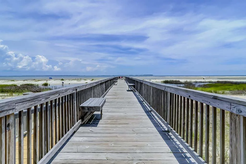 A wooden boardwalk extends across grassy dunes toward the beach.