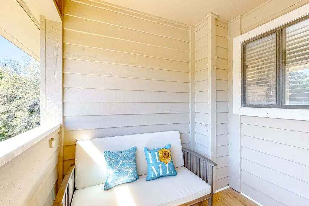 A bright enclosed porch with a cushioned bench and windows overlooking trees.