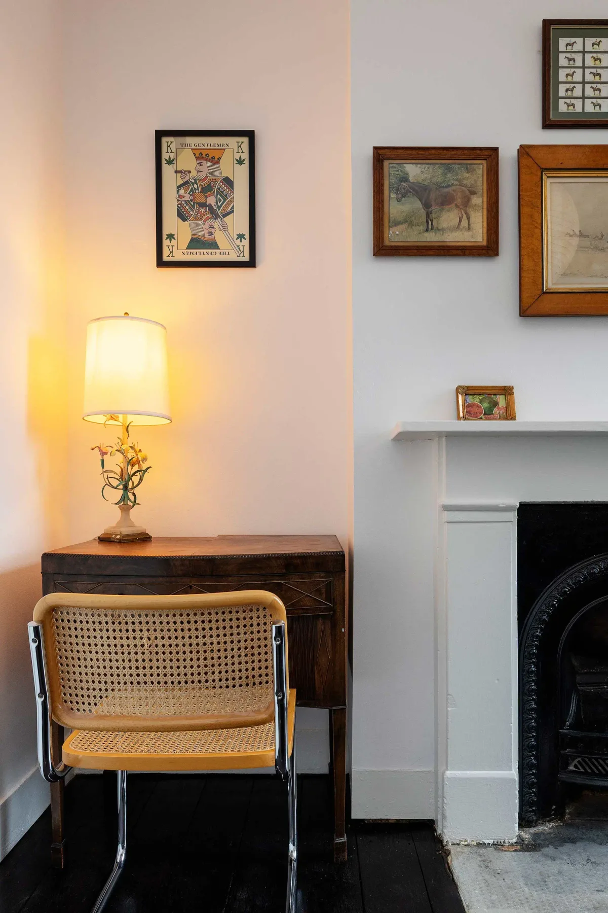 Una esquina de sala de estar con escritorio, silla, lámpara encendida y chimenea.