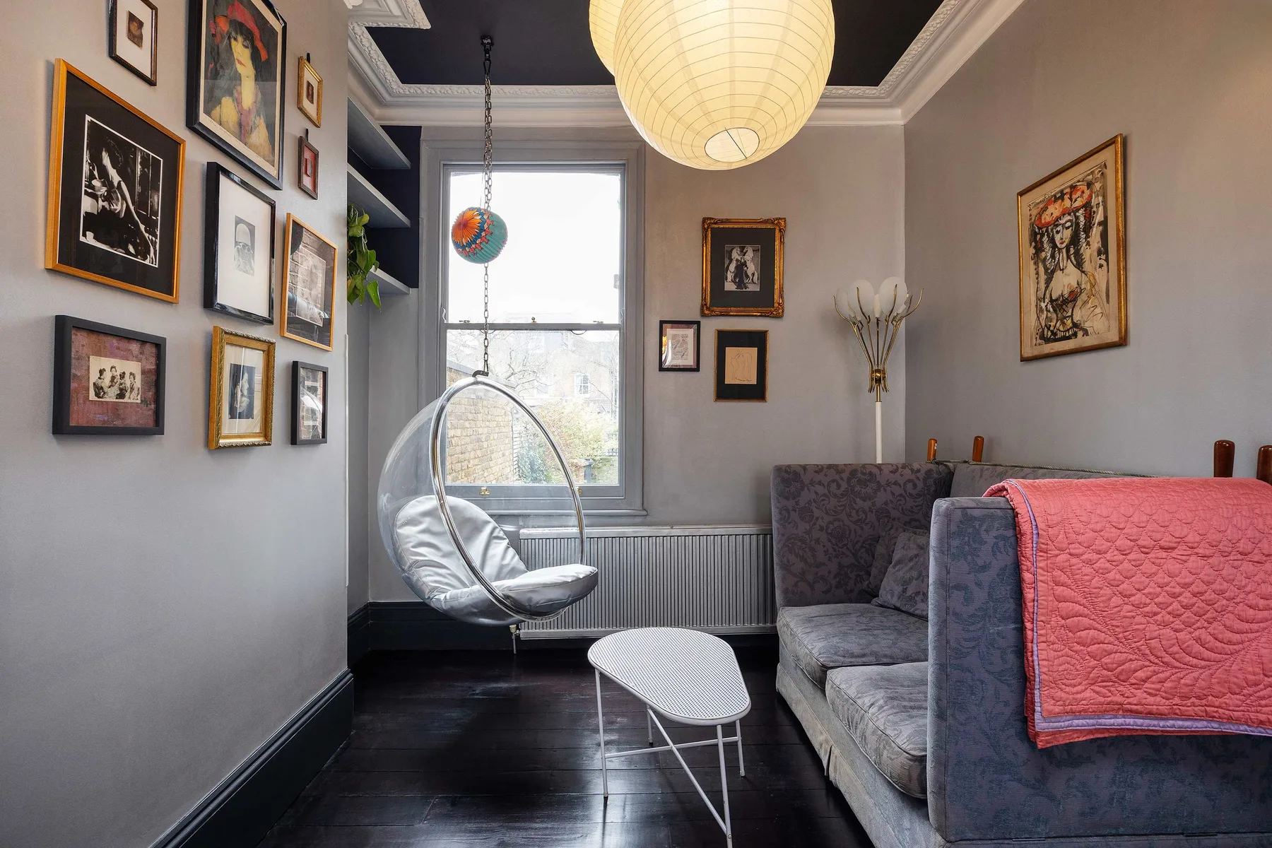 Una sala de estar con un sofá gris, una silla colgante y cuadros en las paredes.