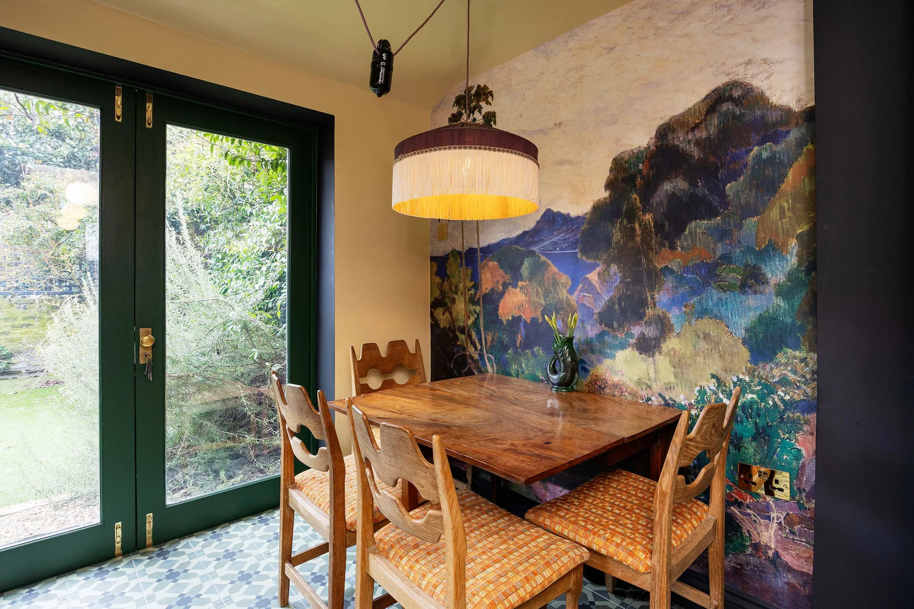 Un comedor con una mesa de madera, sillas y un mural colorido de paisaje.