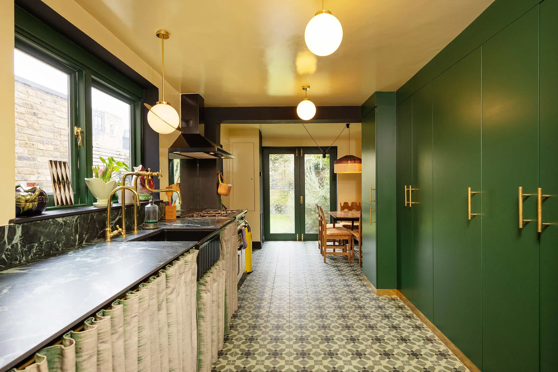 Una cocina alargada con gabinetes verde oscuro, una encimera y suelo estampado.