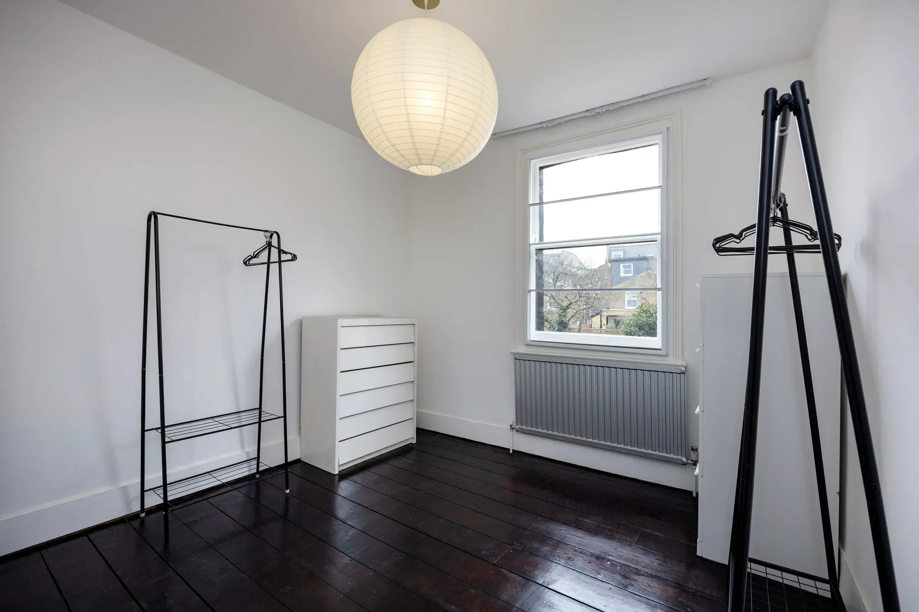 Una habitación luminosa con percheros y una ventana sobre un radiador.