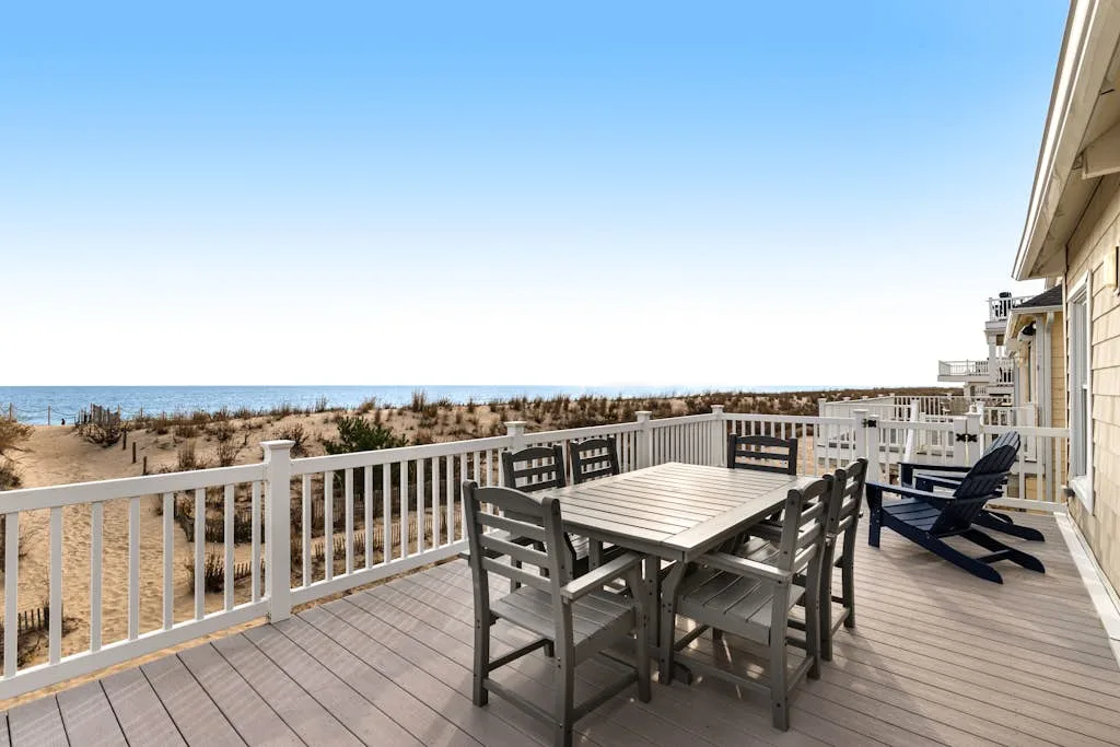 A seaside deck with a dining table and chairs overlooking the beach.