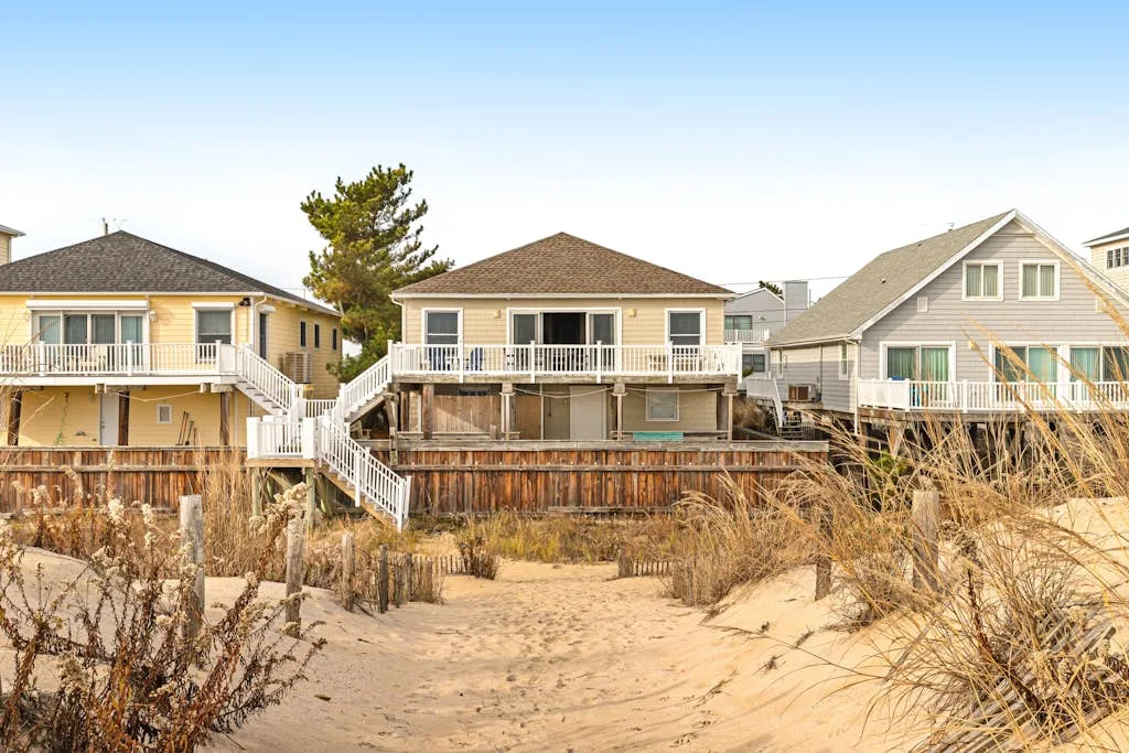 A sandy path through dune grass leads toward beachfront houses.