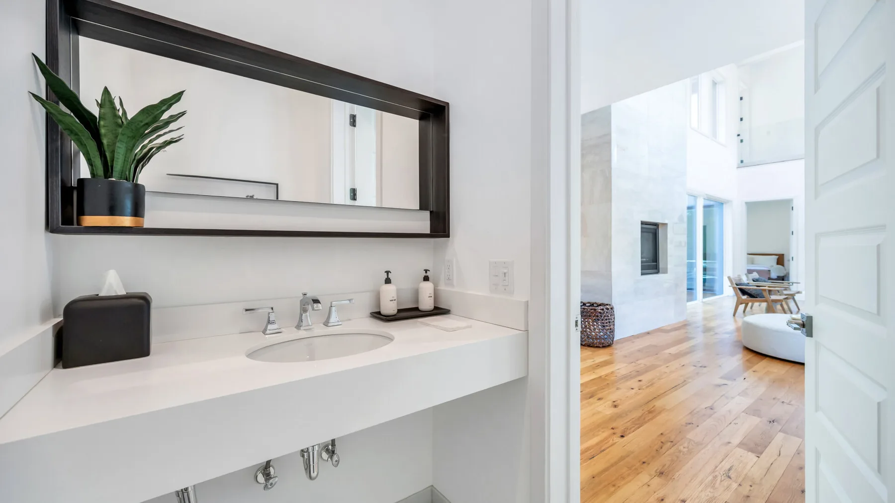 A bathroom vanity with a wide mirror opens onto a bright adjoining room.