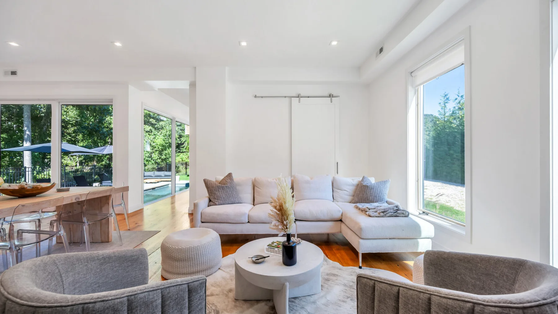 A bright living room with light seating, a round coffee table, and large windows.