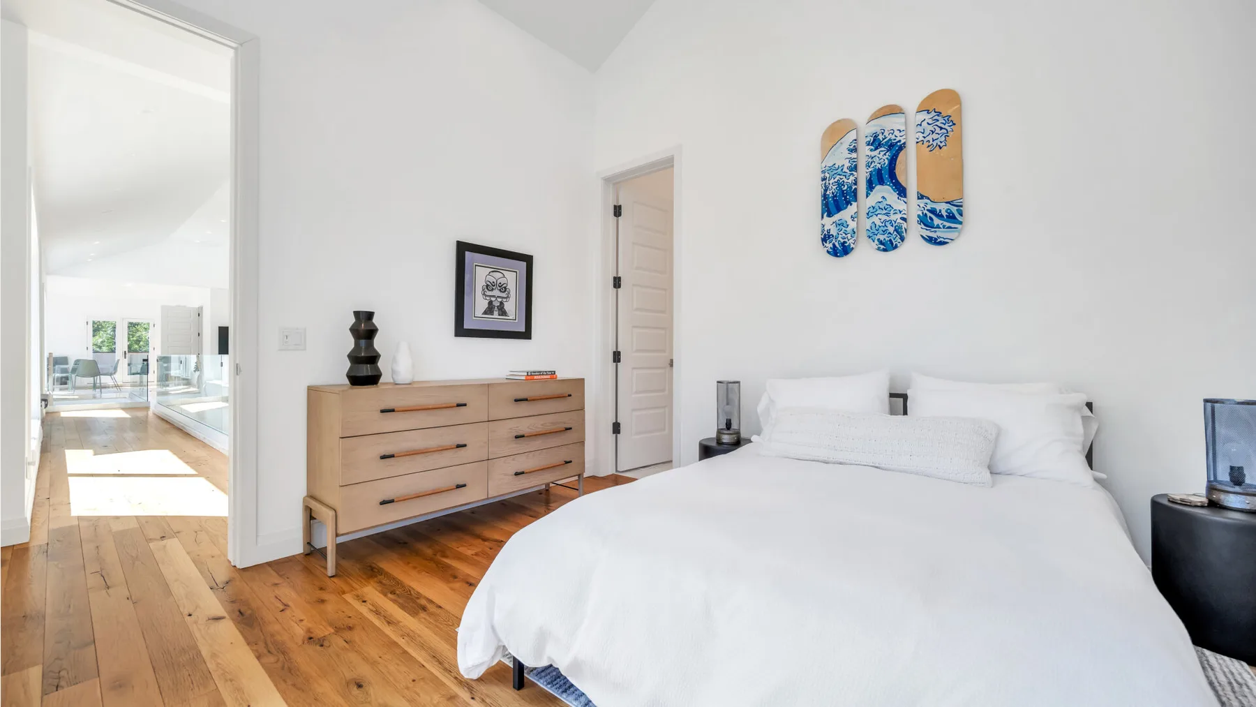 A bright bedroom with a white bed and a wooden dresser.