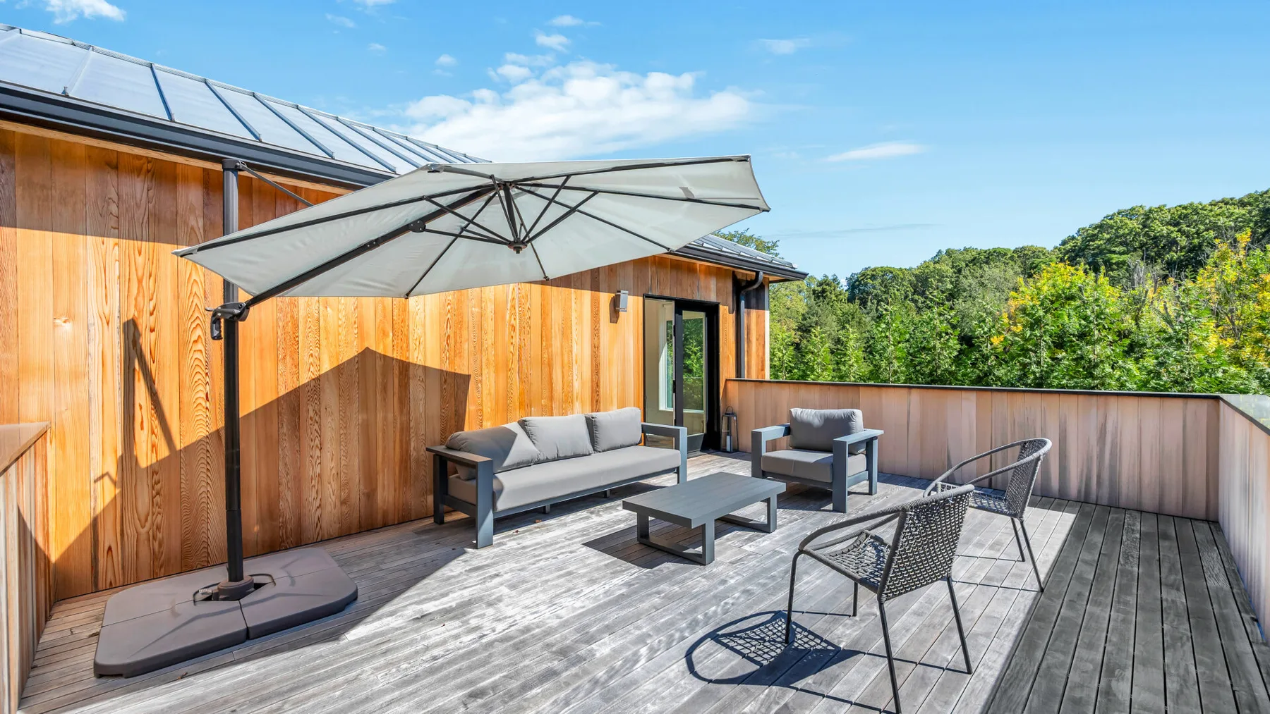 A sunny wooden deck has outdoor seating beneath a large umbrella.