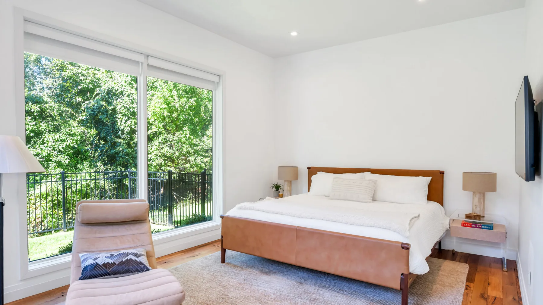 A bright bedroom with a bed beside large windows overlooking greenery.