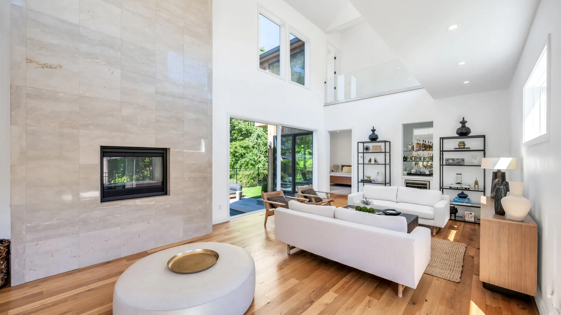 A bright living room with white seating, a fireplace, and tall windows.