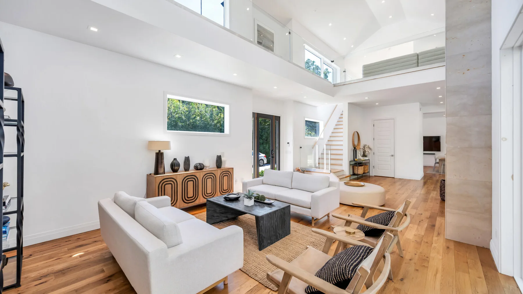 A bright open-plan living room with white seating and a staircase to the upper level.