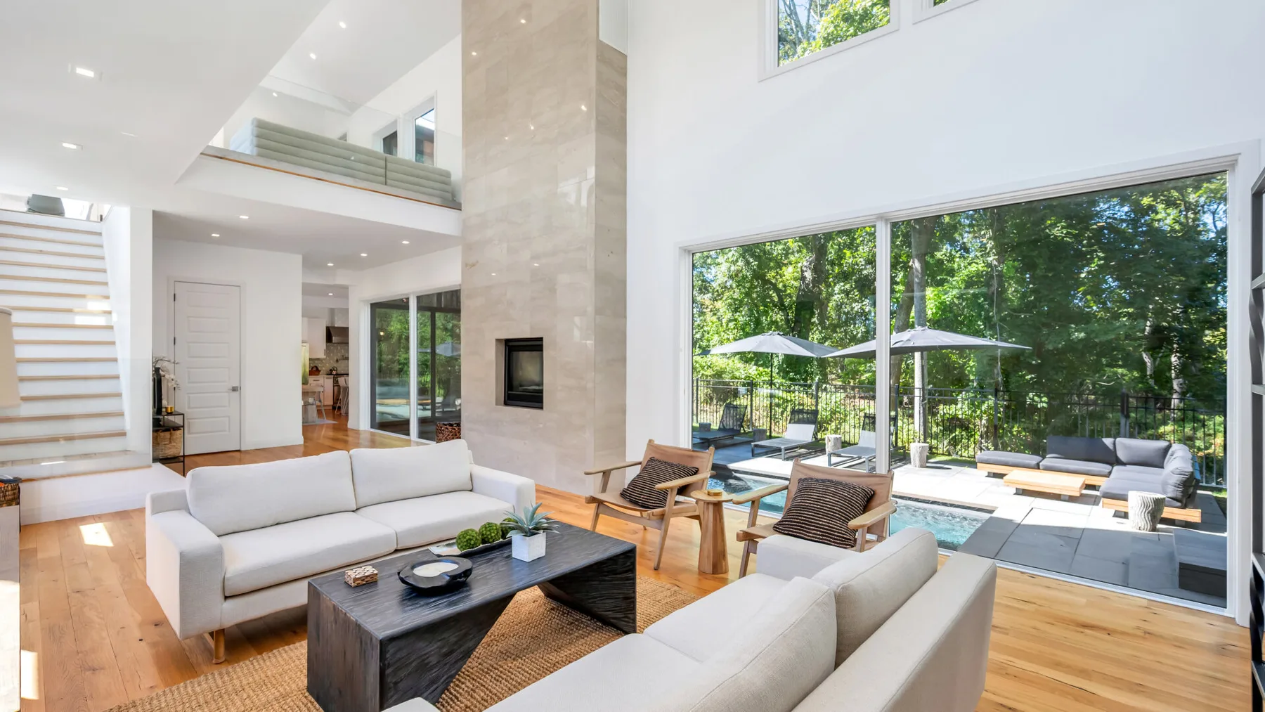 A bright open-plan living room with seating beside large windows overlooking a garden.