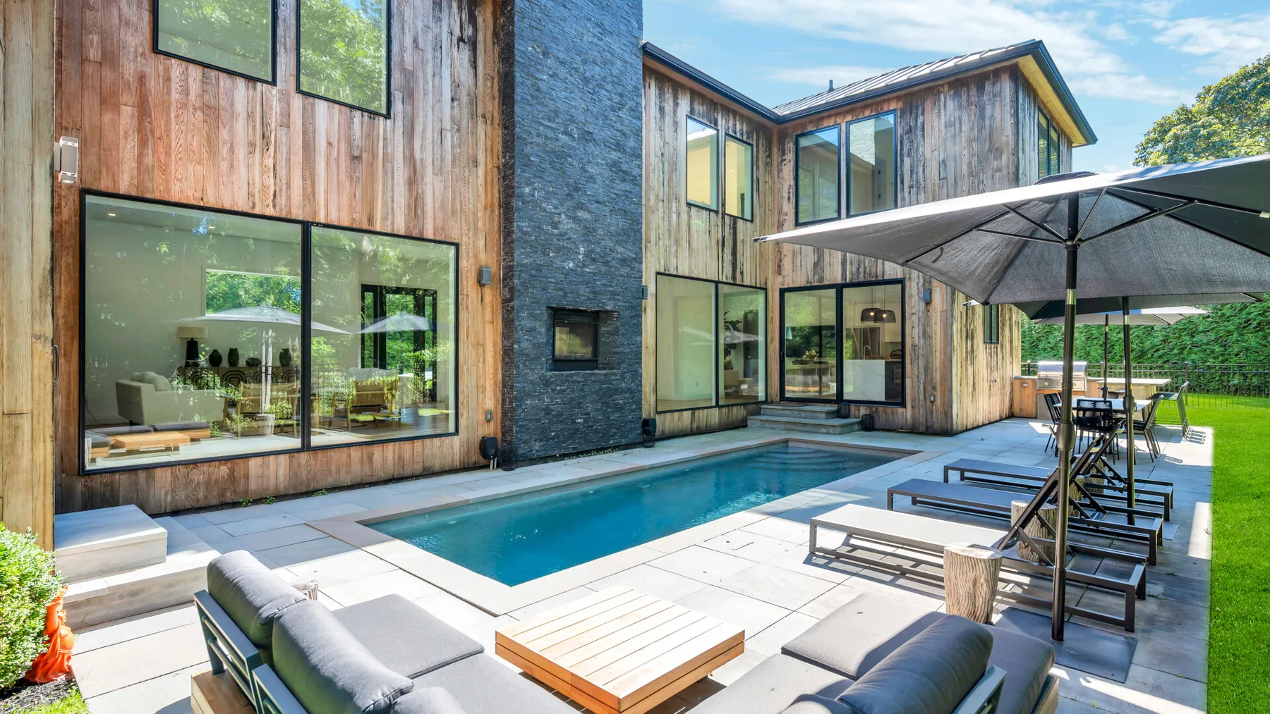 Una casa moderna da a un patio con una piscina rectangular y asientos al aire libre.